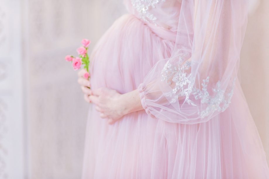Beautiful pregnant woman in rich pink dress holds hands on her b
