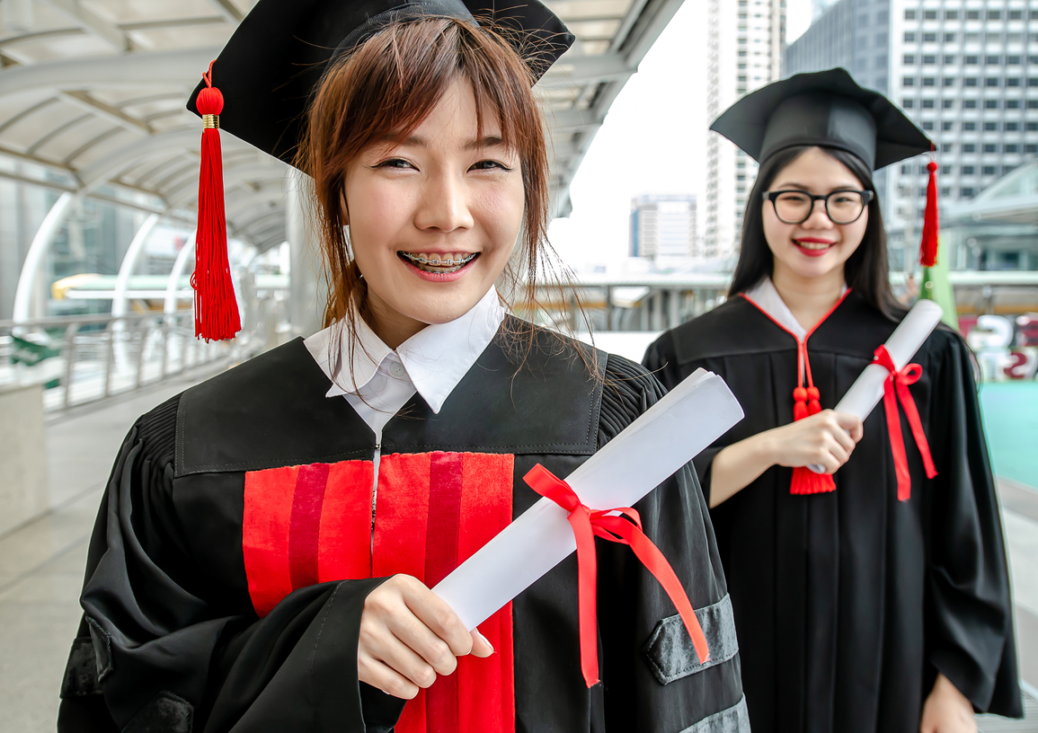 two university students asian woman wear gowns hold graduation